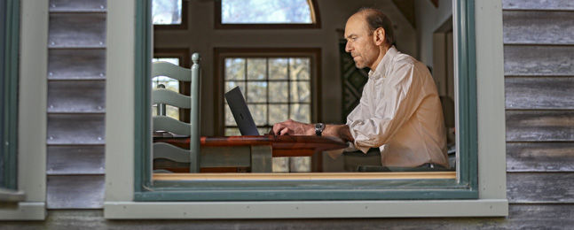 A photo of James Pustejovsky, taken outside his home, shot through an open window, showing him at work on his laptop.